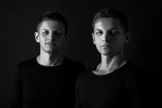 Two attractive positive young twin brothers standing dressed in black sweaters on black background. Black and white photography