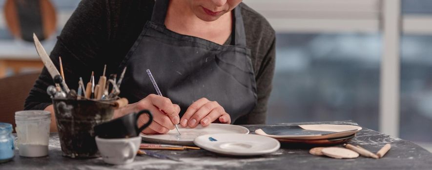 Woman decorating plate with handmade pattern using brush