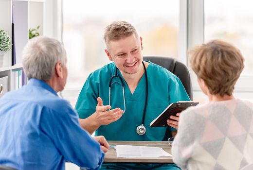 Physician talking to mature couple in cabinet during appointment in medical clinic