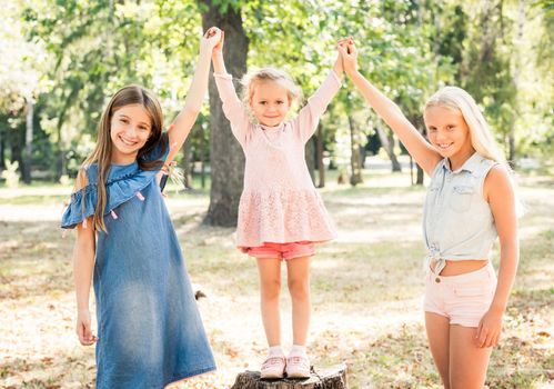 Pretty smiling little girls stand with joyfully raised hands in a sunshine autumn park