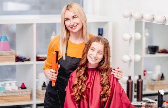 Portrait of hairdresser and model girl with curles after hairstyle together. Professional hairdo in beauty salon