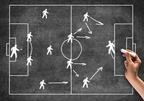 Businessman hand with chalk draws scheme of game. Freehand illustration on blackboard. Planning strategy and tactics of next game. Soccer field with players pictograms. Team game competition concept