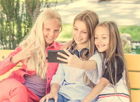 Teenage girls making selfie outdoors while sitting on the bench. Happy friends in the park on a sunny day. Happy friendship concept