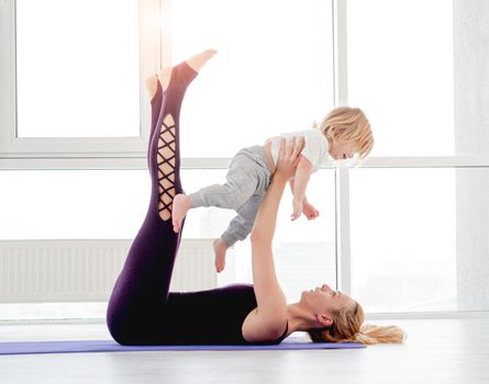 Family yoga workout at home. Blond mother exercising and holding her son in outstretched arms above herself