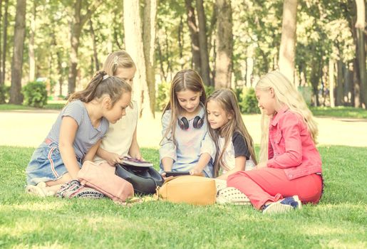 Friendly teens sitting with notebooks on the grass in the park