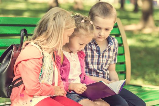 Little kids watching notes on the green bench in sunshine park