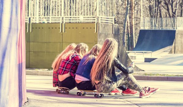 Back view of four blonde girls sitting on longboards in the skatepark. Young sporty girls in the city