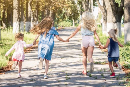 Little blond girls running on the sunshine autumn alley by holding hands