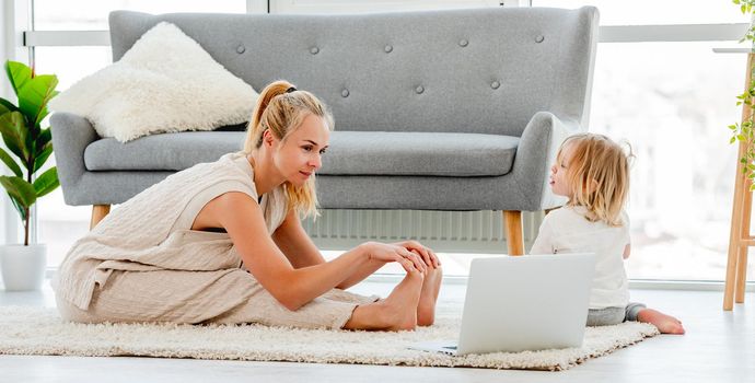 Mother exercising with child at home and watching online video workout at laptop