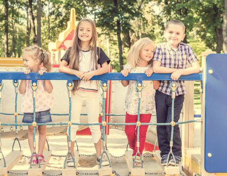 Little cute blond girls and boy on the colourful playground bridge