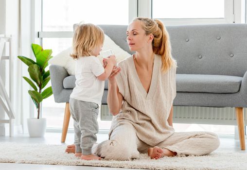 Beautiful young blond mother sitting on the fllor with child son and gives him water in the glass