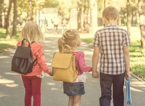 Little pupils walking home from school across the sunshine park