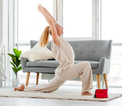 Blond girl staying in asana during morning yoga workout online on tablet