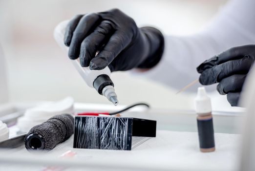 Permanent makeup master preparing materials for eyebrows tattoo. Closeup view of cosmetologist hands with tube of paint