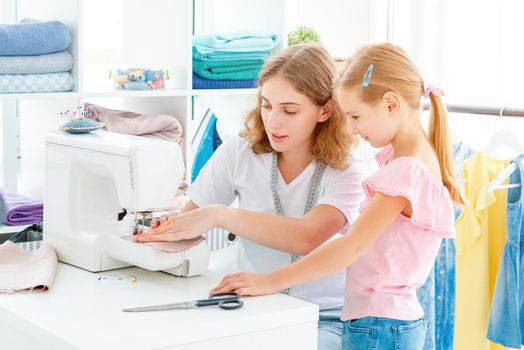 Little girl is taught to sew by teacher at class