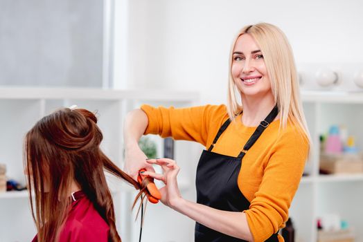 Hairdresser making hairstyle with curls to young model using a hair iron and smiling