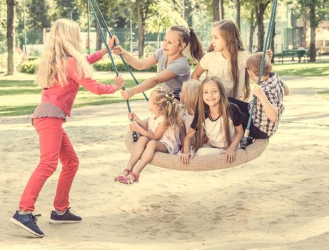 Blond girl swinging little smiling kids on the big swing