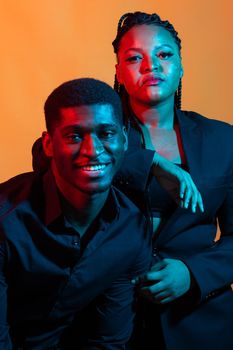 Portrait of young african american couple in love posing at studio dressed in classic clothes. Neon light