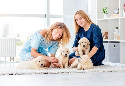Beautiful girls playing with retriever puppies in light room