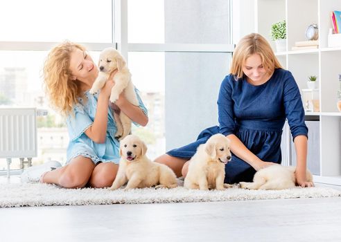 Cheerful girls playing with puppies at home