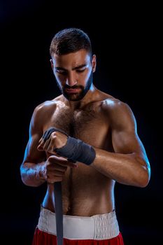 Boxer preparing her gloves for a fight. Photo of muscular man strapping up hands on black background. Strength and motivation. Studio shot