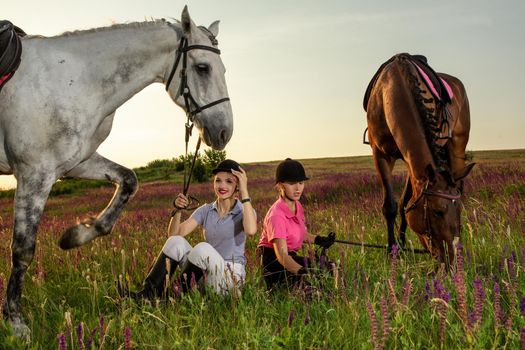 Two woman and two horses outdoor in summer happy sunset together nature. Taking care of animals, love and friendship concept.