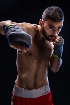 The boxer is ready to deal a powerful blow. Photo of muscular man with strong hands and clenched fists in blue stripes on black background. Strength and motivation. Studio shot