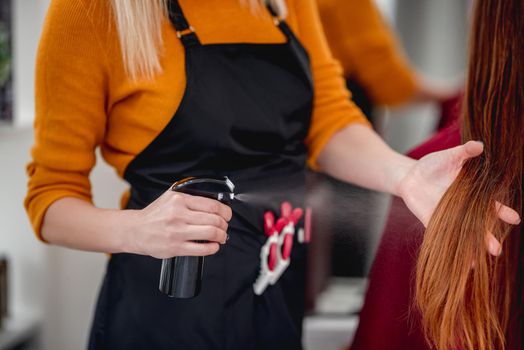 Closeup view hairdresser spraying long hair of client in beauty salon