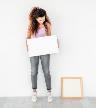 Cute girl standing near frame with empty canvas in her hands