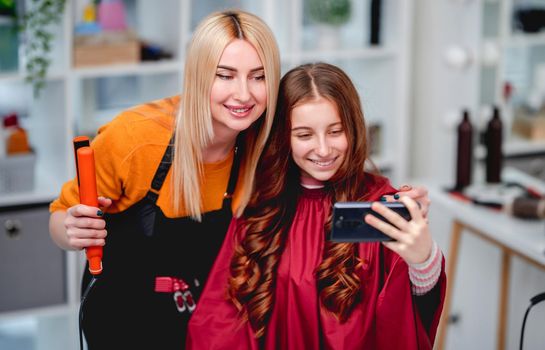 Selfie of hairdresser blond woman with client beautiful girl model after professional curls hairstyle