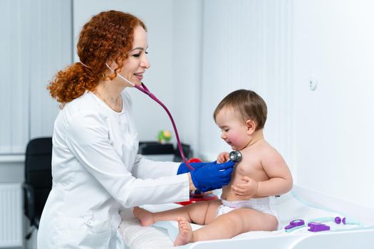 Pediatrician doctor concept. Children medical care. One year old baby girl examined by female pediatrician in clinic office. Child visiting doctor for health check-up. Doctor examine little patient.