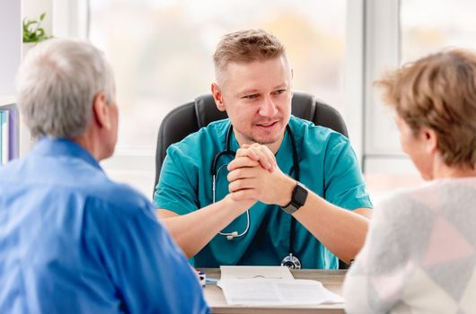 Physician talking to mature couple in cabinet during appointment in medical clinic
