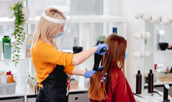 Hairdresser care about long hair of client model girl wearing masks. Hairstyle during pandemy time