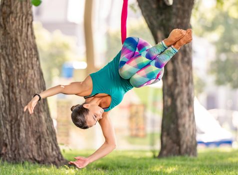 Sport girl practicing fly yoga in hammock at nature and keeping balance in the air with head down. Young woman doing aero fitness gymnastic stretching outdoors