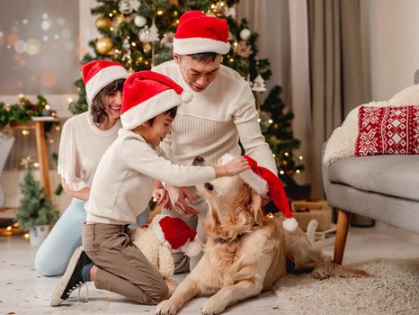 Happy family posing near christmas tree while golden retriever dog is passing by in front of camera