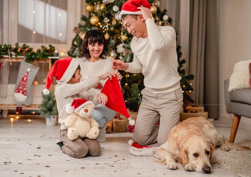 Smiling family putting santa hats while having fun near christmas tree at home