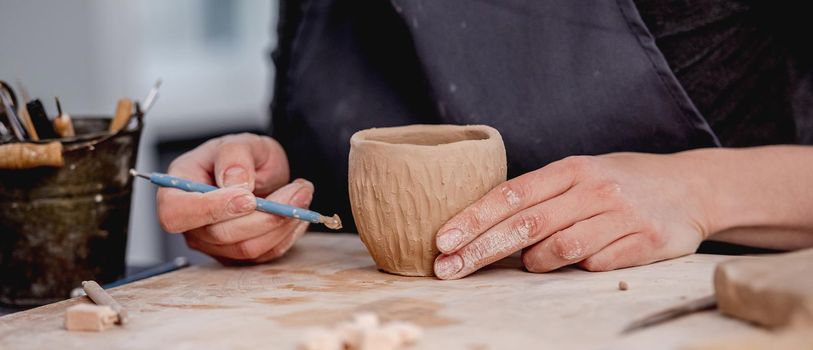 Potter using carving tool on mug making design