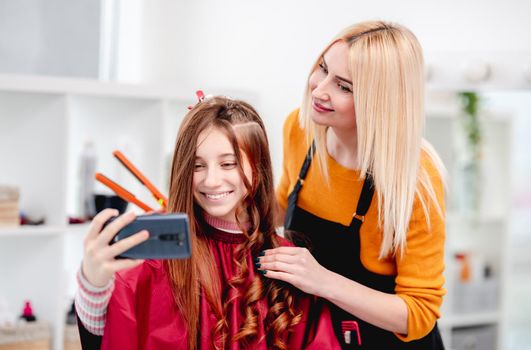 Selfie of beautiful young model with hairdresser blond woman during making curls hairstyle