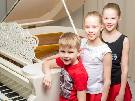 A cheerful company of children near a white grand piano. The concept of music education, children's holidays.