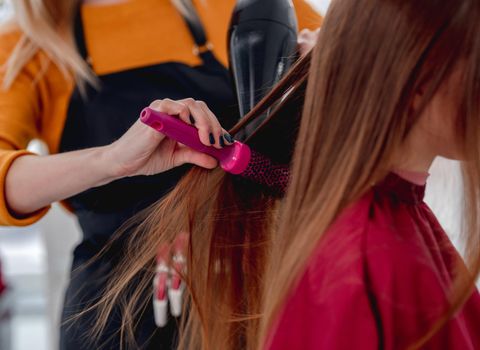 Closeup view of streightening long hair with hairdryer and brush. Professional stylist care about client hairstyle