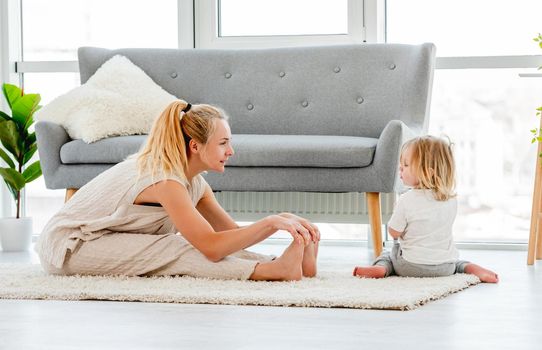 Beautiful blond woman stretch her legs on the floor and looking at her child son