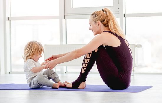 Mother and son sitting on the floor and practicing partner family yoga together at home
