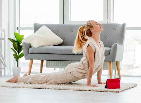 Girl staying in Upward facing dog Urdhva Mukha Svanasana asana during online yoga class with tablet at home. Workouts in quarantine