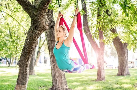 Sport girl practicing fly yoga in hammock at nature and stretching her body. Active woman during aero gymnastics outdoors