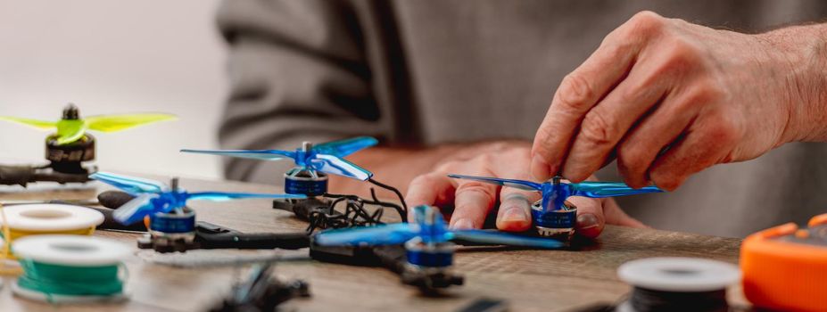 Workplace of service man repairing quadcopters. Closeup view of hands during drone fixing process