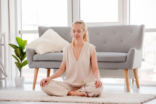 Blond woman meditates sitting on the floor at home with harmonic smile on her face