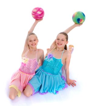 Two cheerful little girls gymnasts in competitions, perform exercises with the ball. The concept of children's sports, fitness, healthy lifestyle. Isolated on white background.