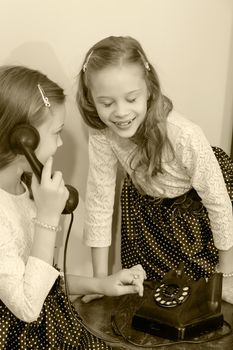 Two elegant girls sisters in beautiful dresses, talking on old phone. Retro style.Black-and-white photo. Retro style.