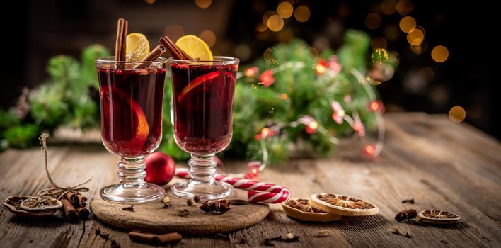 Glass cups with aromatic red mulled wine standing on wooden plate on christmas decoration background
