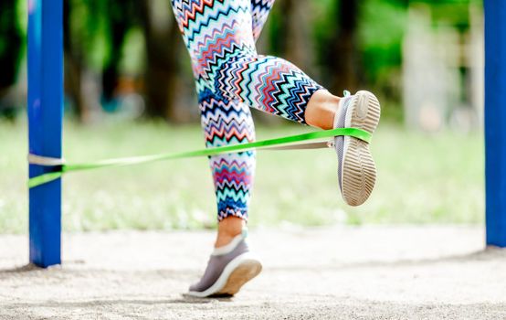 Sport girl with elastic rubber band doing leg workout outdoors. Young woman exercising with fitness equipment